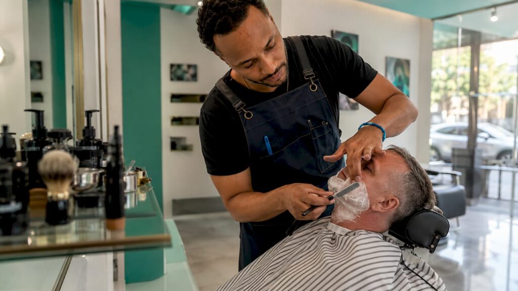 Barber giving straight razor shave in classic barbershop interior