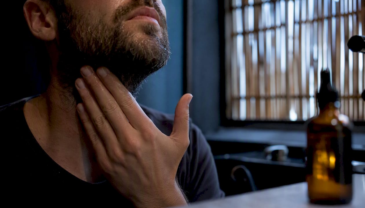 Man applying beard oil to skin under beard