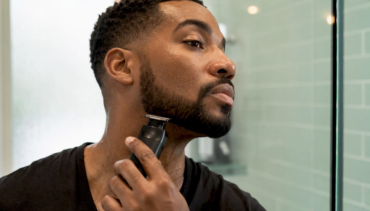 Man shaping beard with trimmer in bathroom
